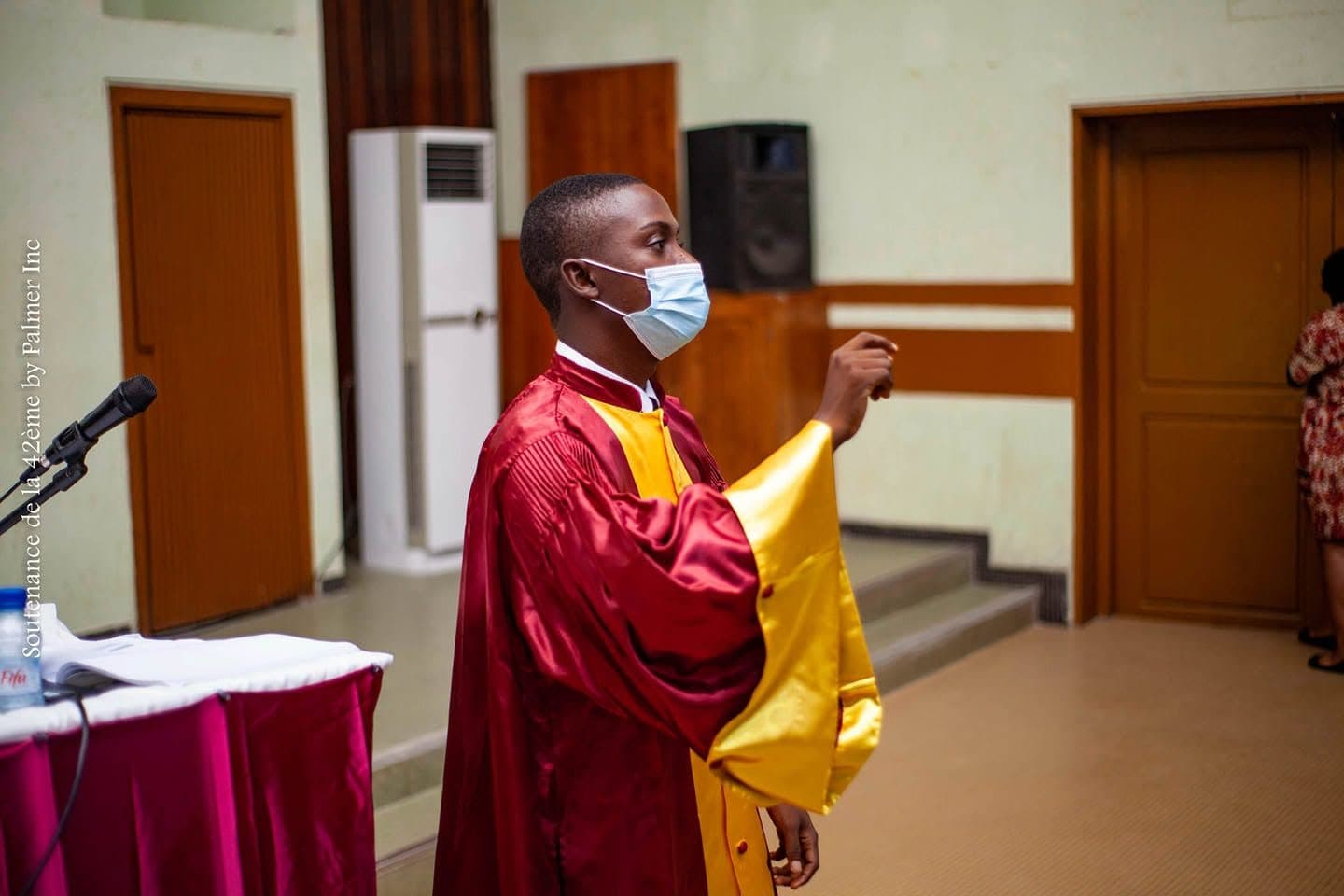 In a bordeaux-and-gold academic gown at the thesis defence, seen in profile.